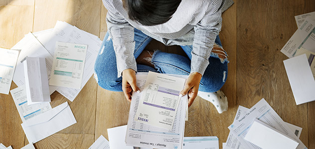 A person sits on a floor surrounded by paper invoices