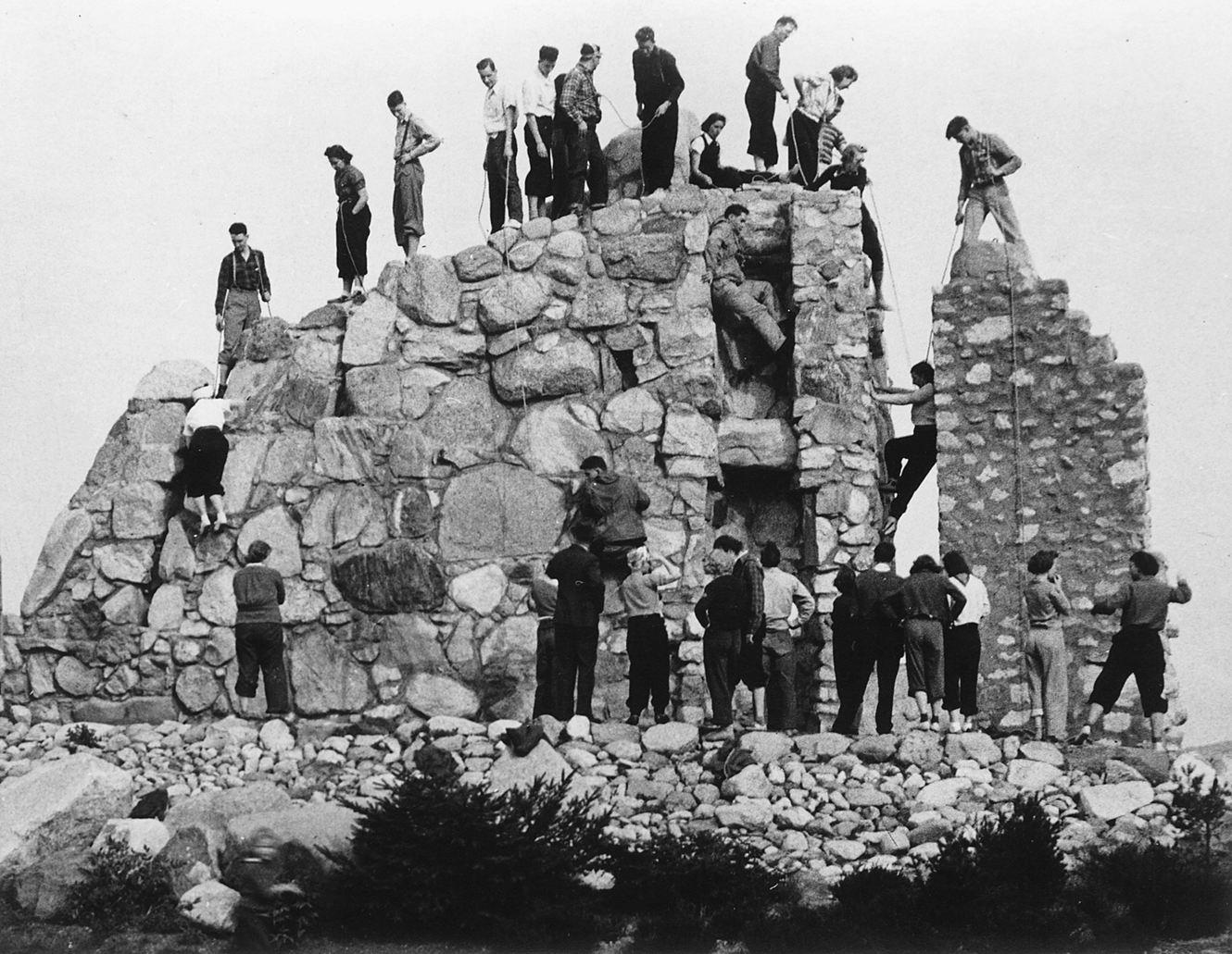 Vintage photograph of a dozen or more men standing atop a man-made rock wall 