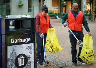 Two volunteers picking up garbage in Cccidental Square with yellow bags, grabbers, and safety vests.