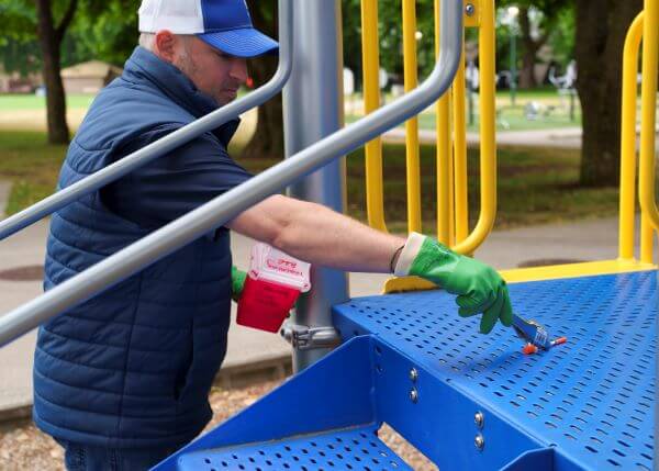 a man with gloves and tongs picking up a syringe from playground equipment.