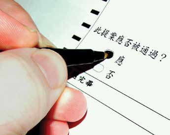 A close-up of a hand holding a black pen filling out an empty circle in a ballot that has Chinese text.