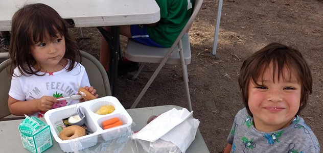 A brother and sister eat at a picnic table