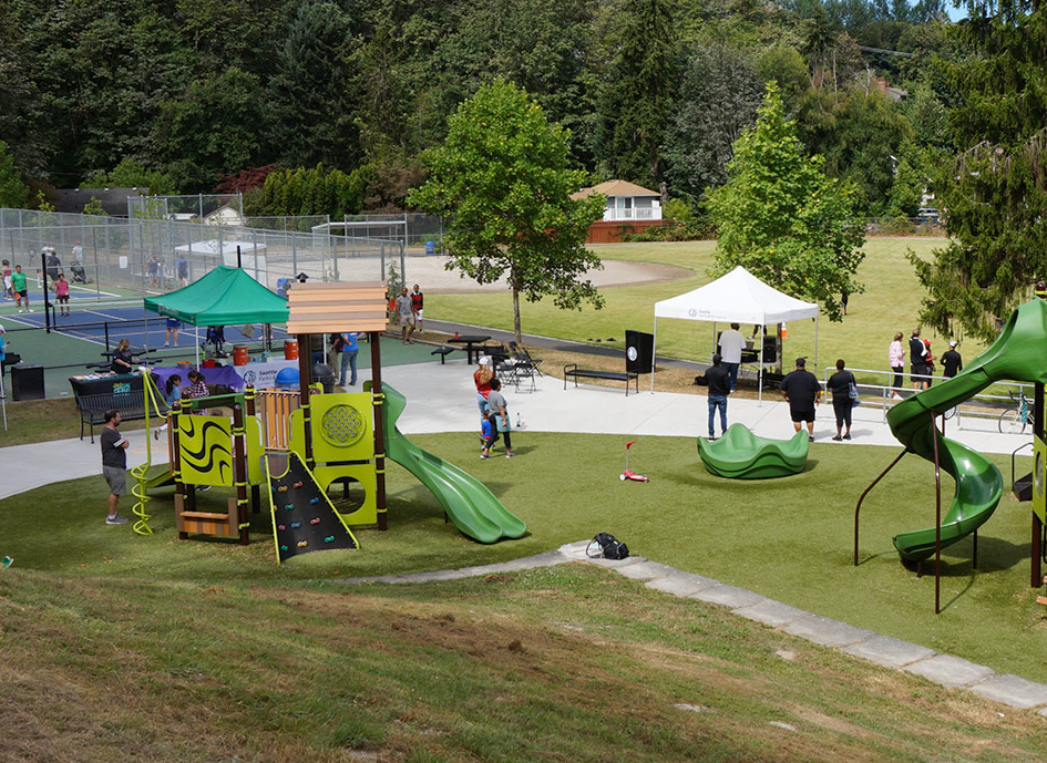 A wide angle shot of a park with tennis courts, meadows and  new playground equipment