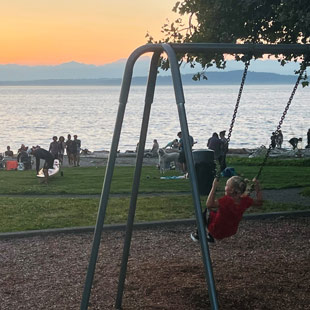 A child on a swingset at sunset in a shoreline green space