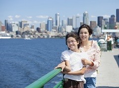 Two girls pose beside the railing of a ferry on Elliott Bay with the Seattle skyline in the background.