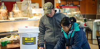 Two business owners work next to a large white plastic bucket labelled "Spill Response Kit".