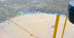 Spilled oil in puddle on gravel roadbed with a rainbow sheen.