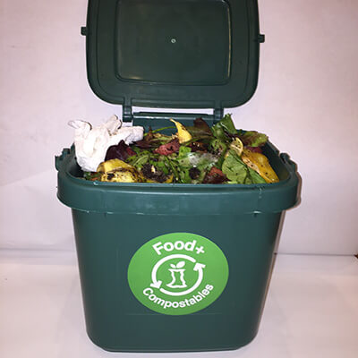 Photo of a counter top size green compost bin filled with food scraps and food-soiled paper.