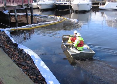Photo of two members of spill response team in a boat close to shore deploying Spill containment equipment.