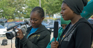 Two teens standing outside holding filming cameras and mics