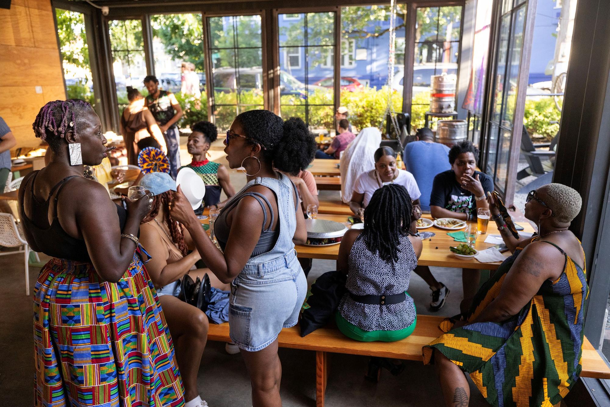 A sunny room with many Black adults chatting and eating at a large table