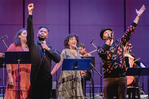 Four singers up on stage, two with their arms extended to the roof.