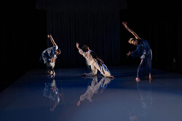 Three Black dancers in various poses that have one arm extended. One is bent at the waist, one kneels, one bends to the side.