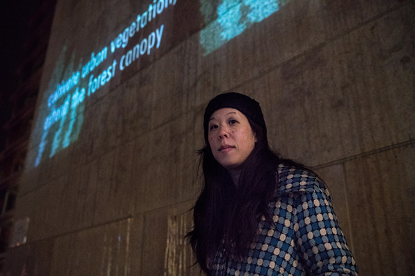 Shin Yu Pai wearing a beanie and flannel. posing in front of a concrete wall. 