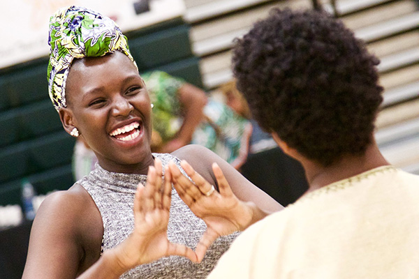 A woman smiling as she creates a diamond symbol with her hands.