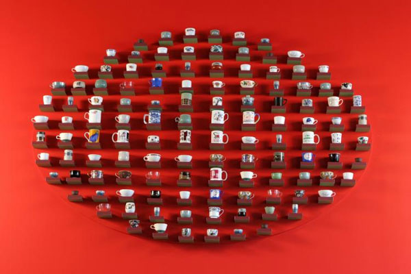 Different teacups on small wooden shelves arranged in an oval against a red wall.