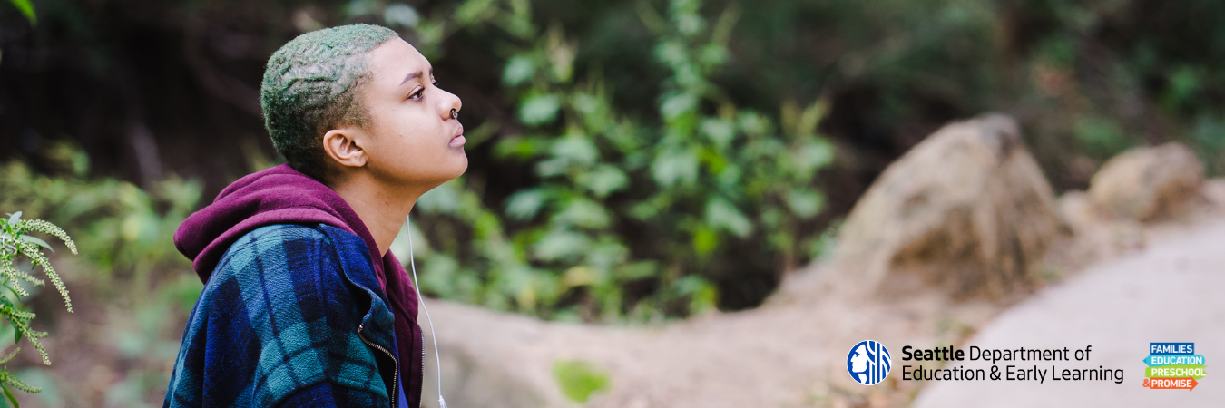 Profile of high school aged youth of color with a thoughtful expression, wearing a plaid shirt, sitting outdoors