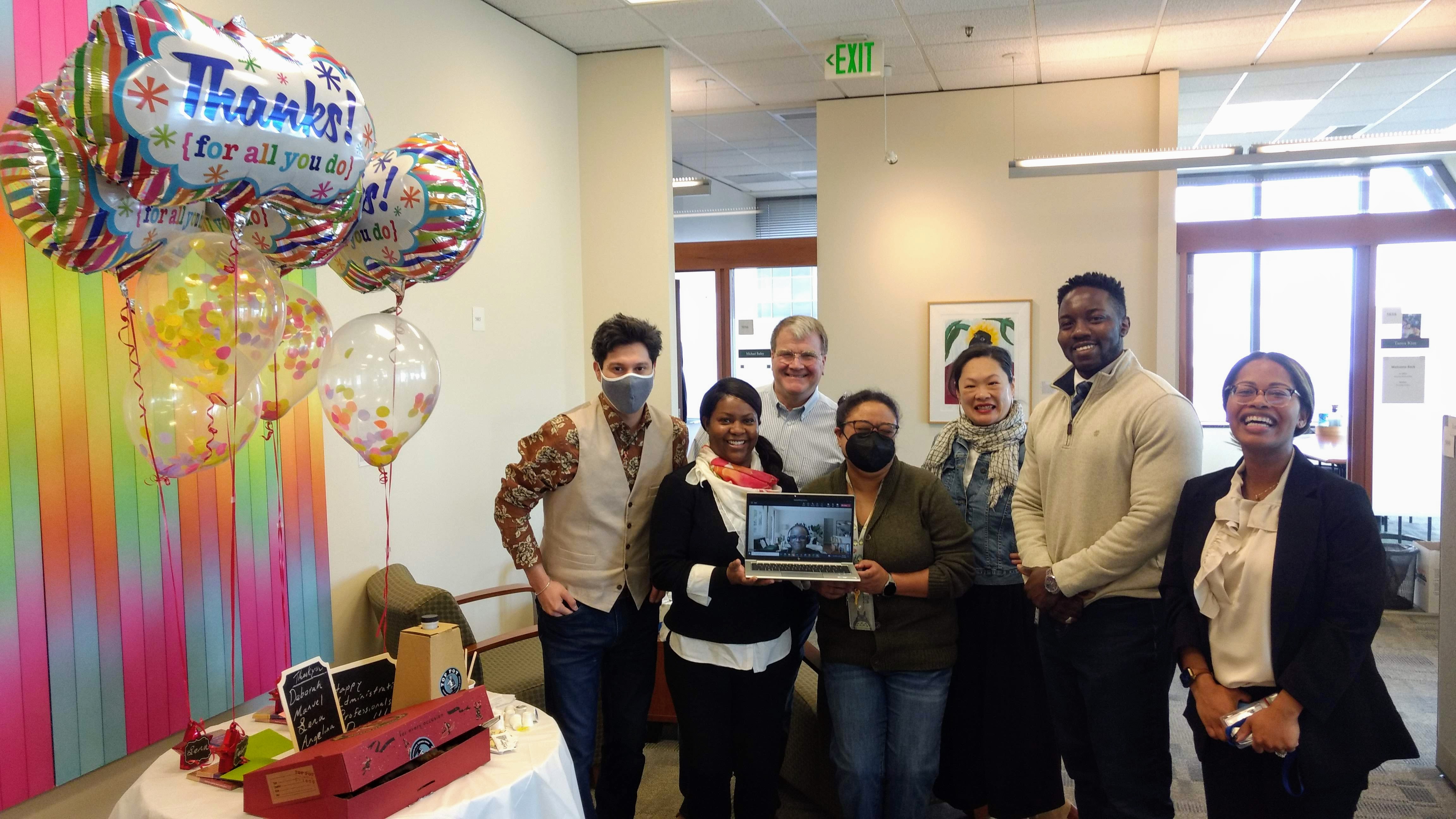 Photo of smiling HSD employees (including a virtual participant seen on a laptop screen) celebrating Admin Professionals Day with balloons and food