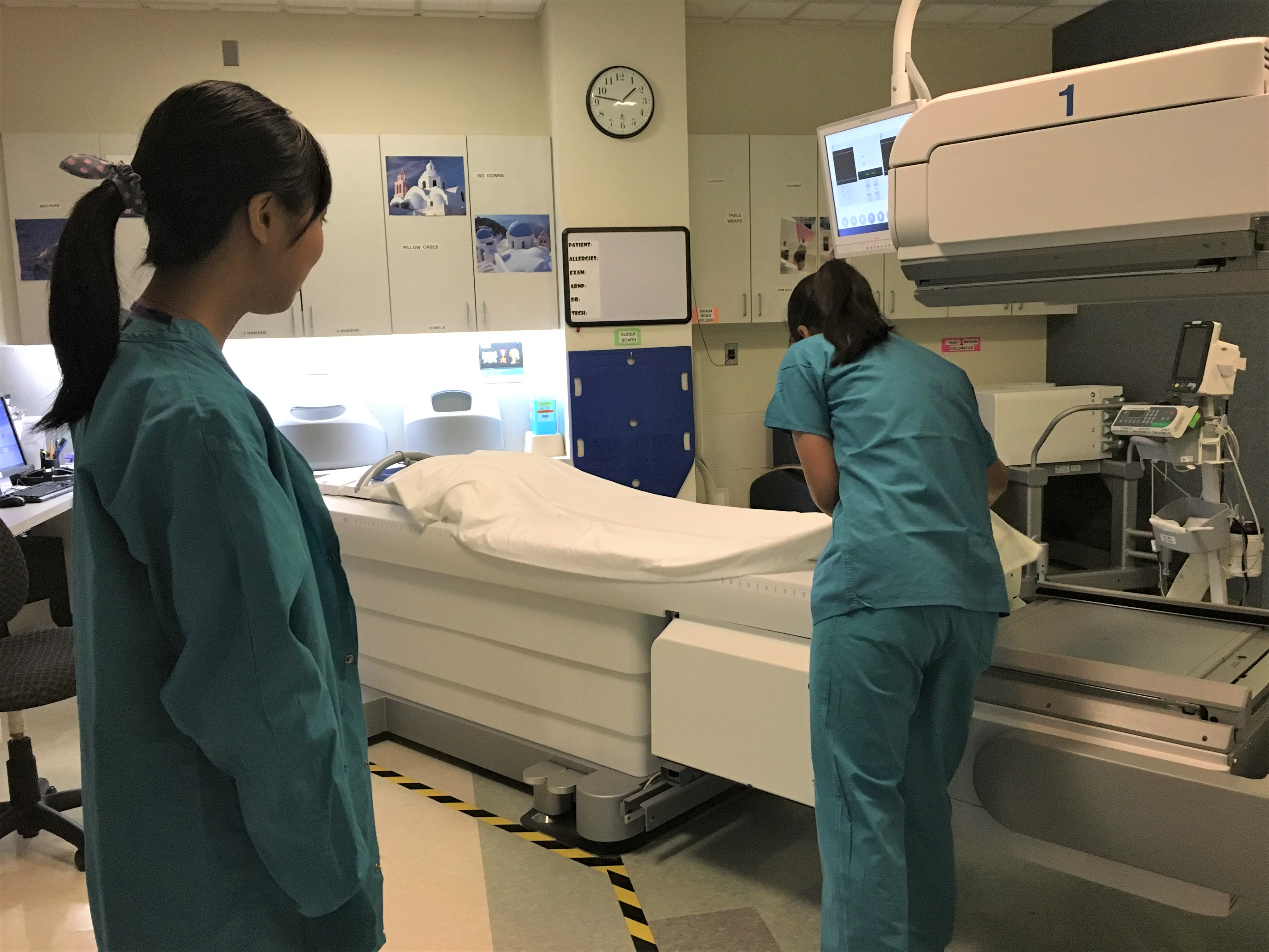 Two interns in blue hospital gowns are shown preparing a bed in a patient room
