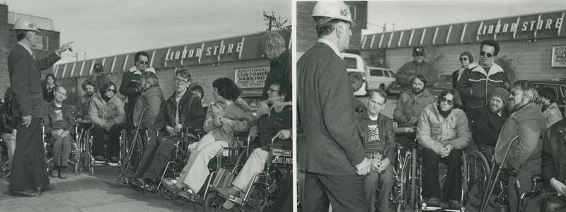 Group of people in wheelchairs listening to a City engineer speak outside a shop.