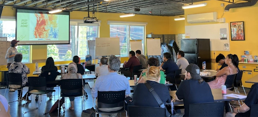Photo of about 15 community members participating in a pilot session of the Curriculum focused on extreme heat. They are seated in a classroom and looking at a slide that shows a heat map of the 2021 heat dome.