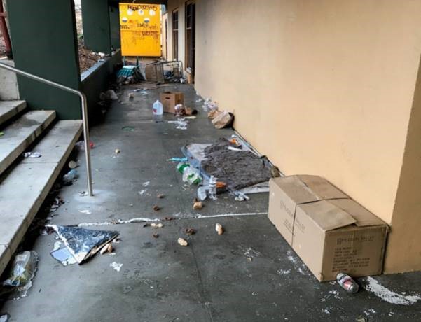 an outdoor breezeway strewn with wet garbage and a shopping cart on its side