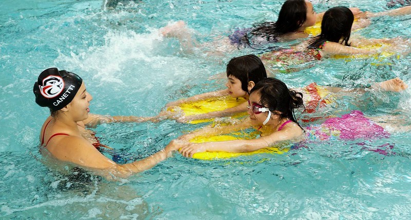 A lifeguard in the water holds hands with two young girls learning to swim with kickboards