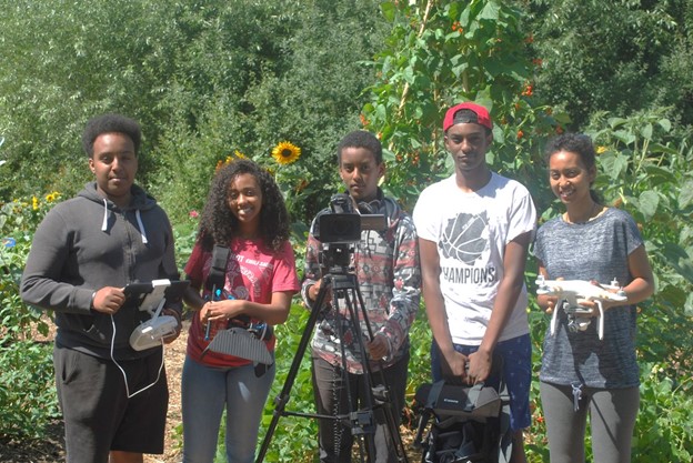 five African American teens holding drone equipment, outside against a background of green shrubs and trees