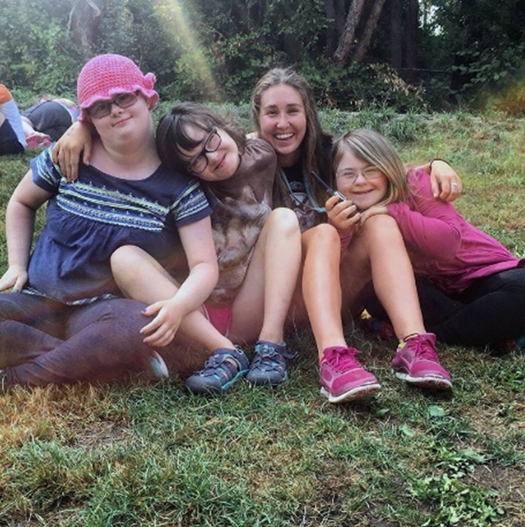 Three young program participants and one adult sitting on a lawn hug each other and smile for the camera
