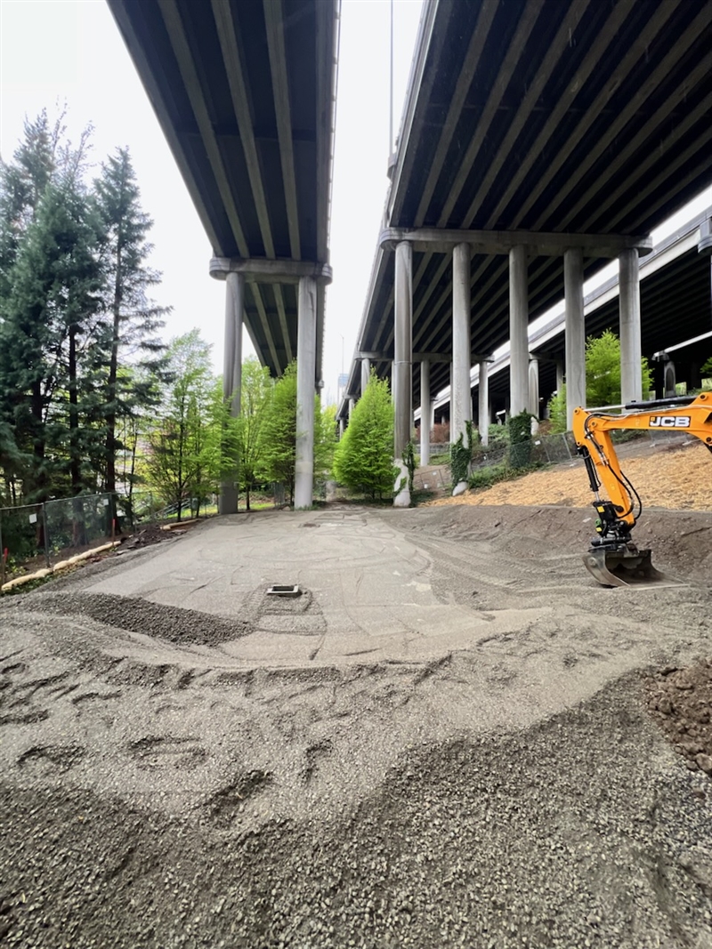Construction photo of pump track, trees surround and a gravel path