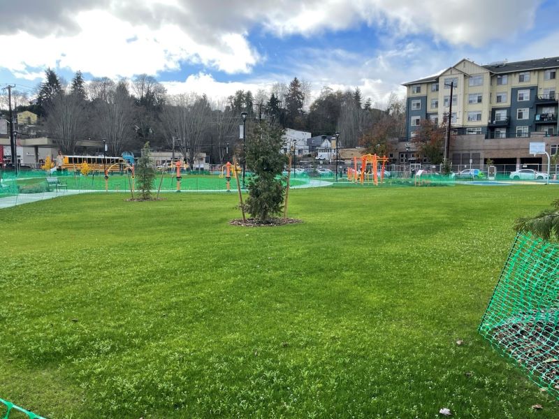 North Rainier Landbanked Site Park - A green lawn with trees, a playground, surrounded by construction fencing
