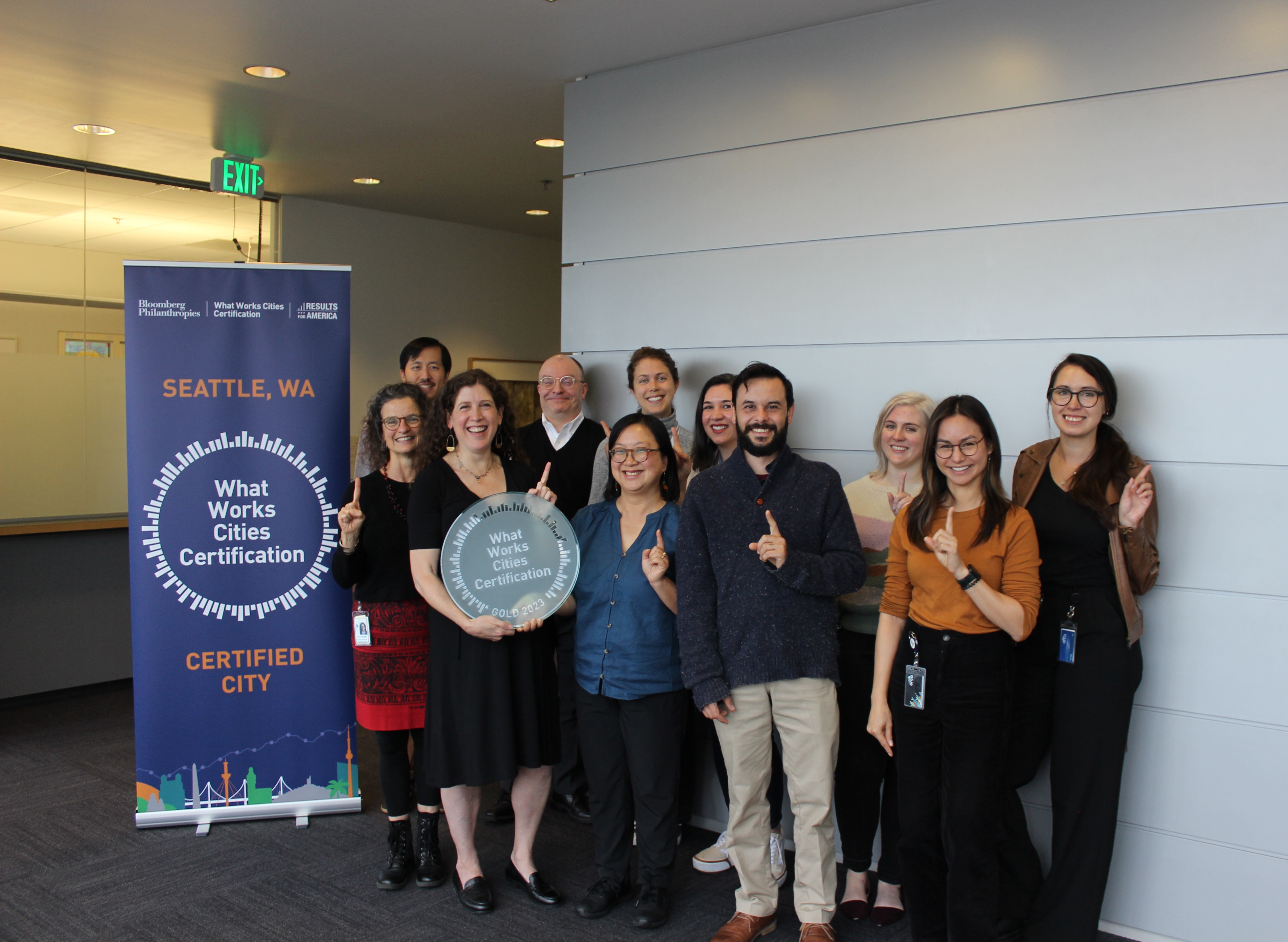 A group of Innovation & Performance employees smile with Director Leah Tivoli holding a What Works Cities Certification plaque