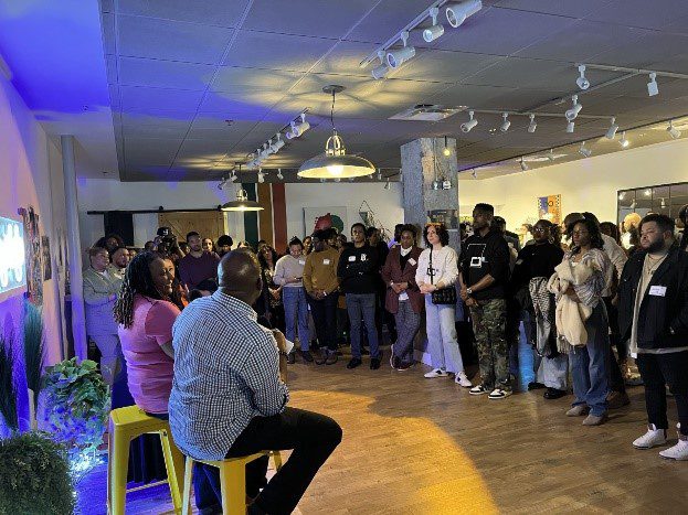A crowd of people stand listening to the panel discussion.