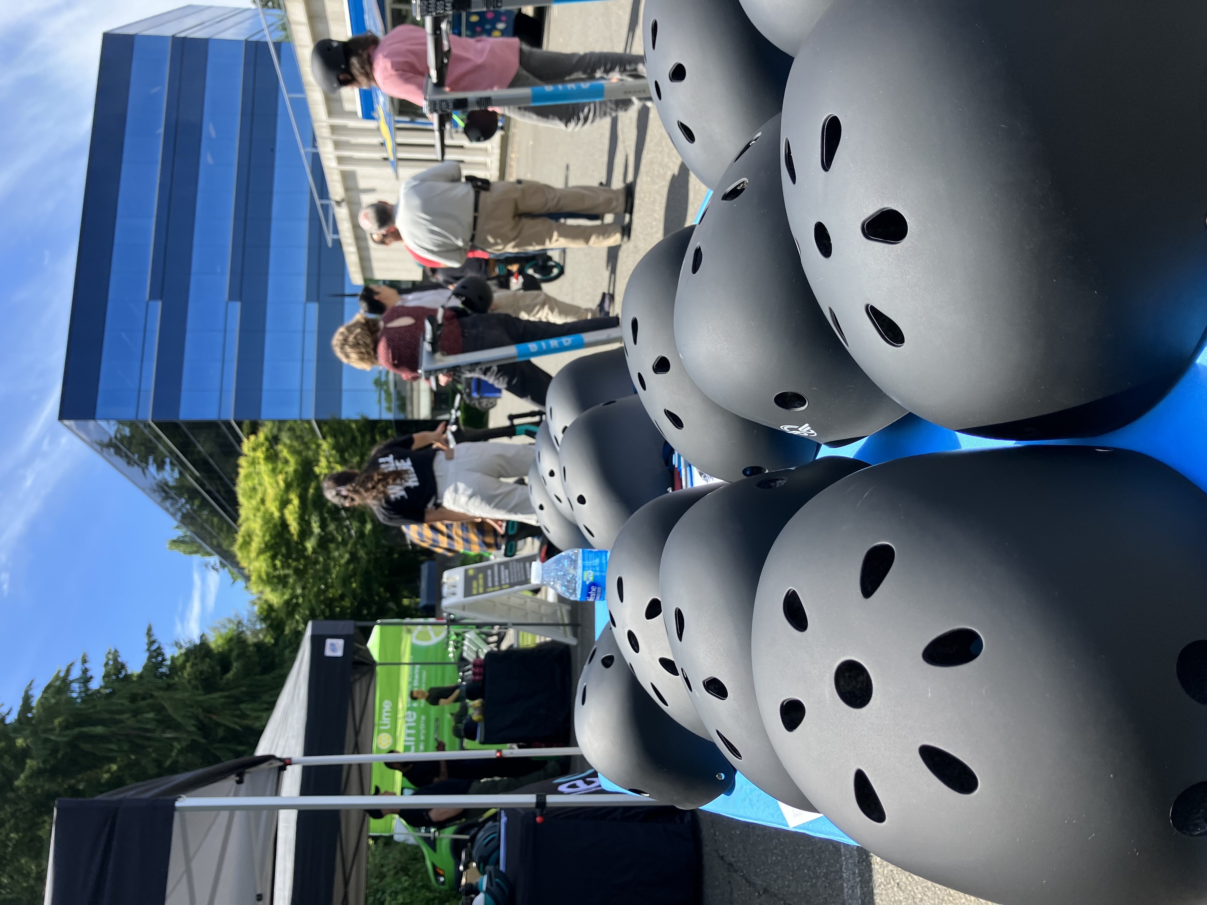 Black helmets on table in front of Bird scooters and people at a Seattle community event