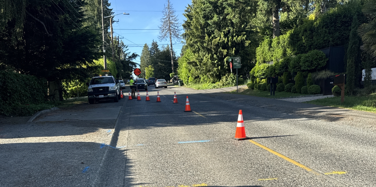 Street view showing traffic cones and a "Slow" paddle sign near NE 104th St and 15th Ave NE. A crew truck and vehicles are present. Trees and homes line both sides of the street