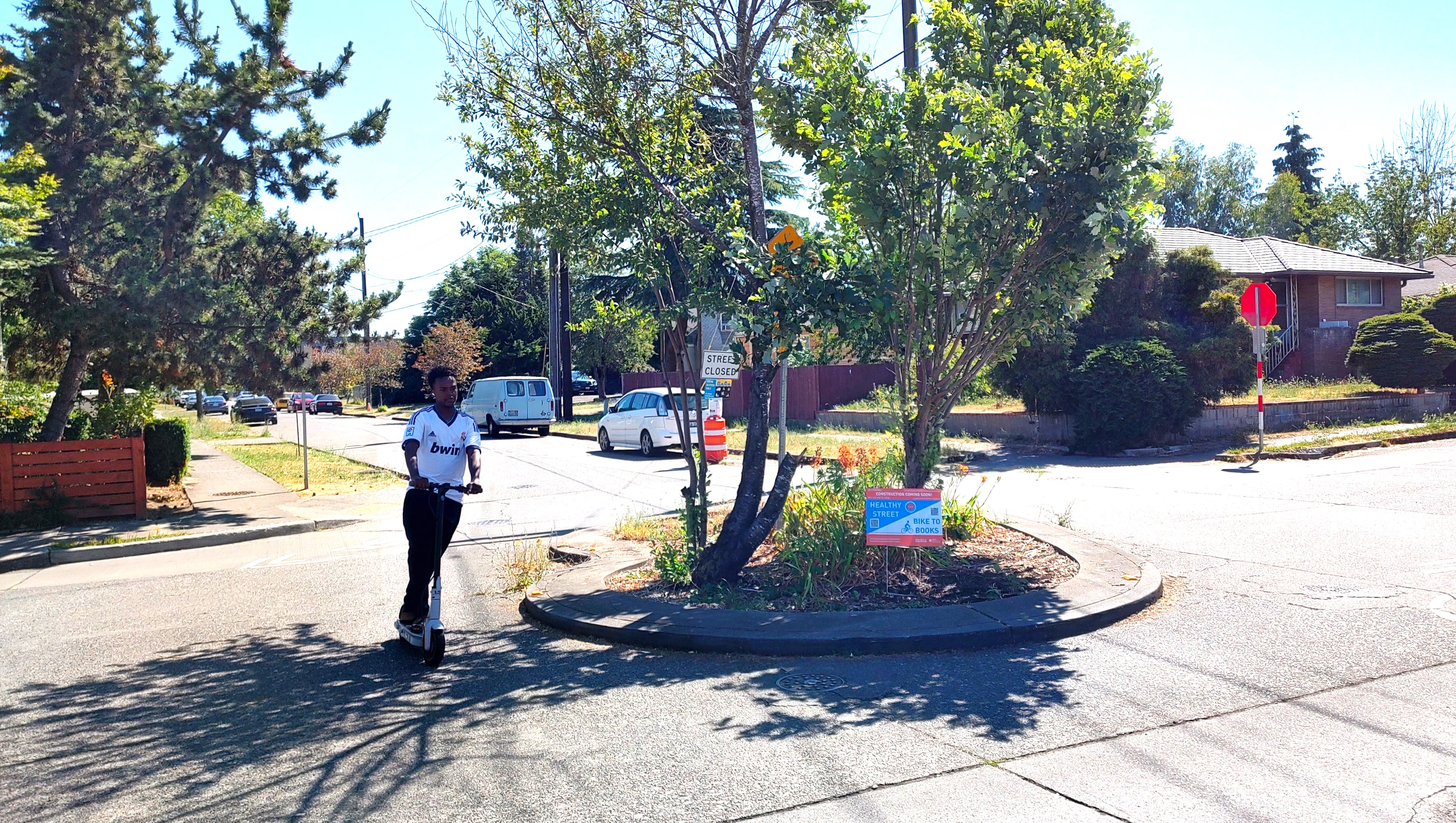 Young man rides past a Construction Coming Soon yard sign on a scooter