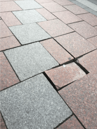 Sidewalk built of gray and pink pavers with one paver able to be moved with foot pressure.