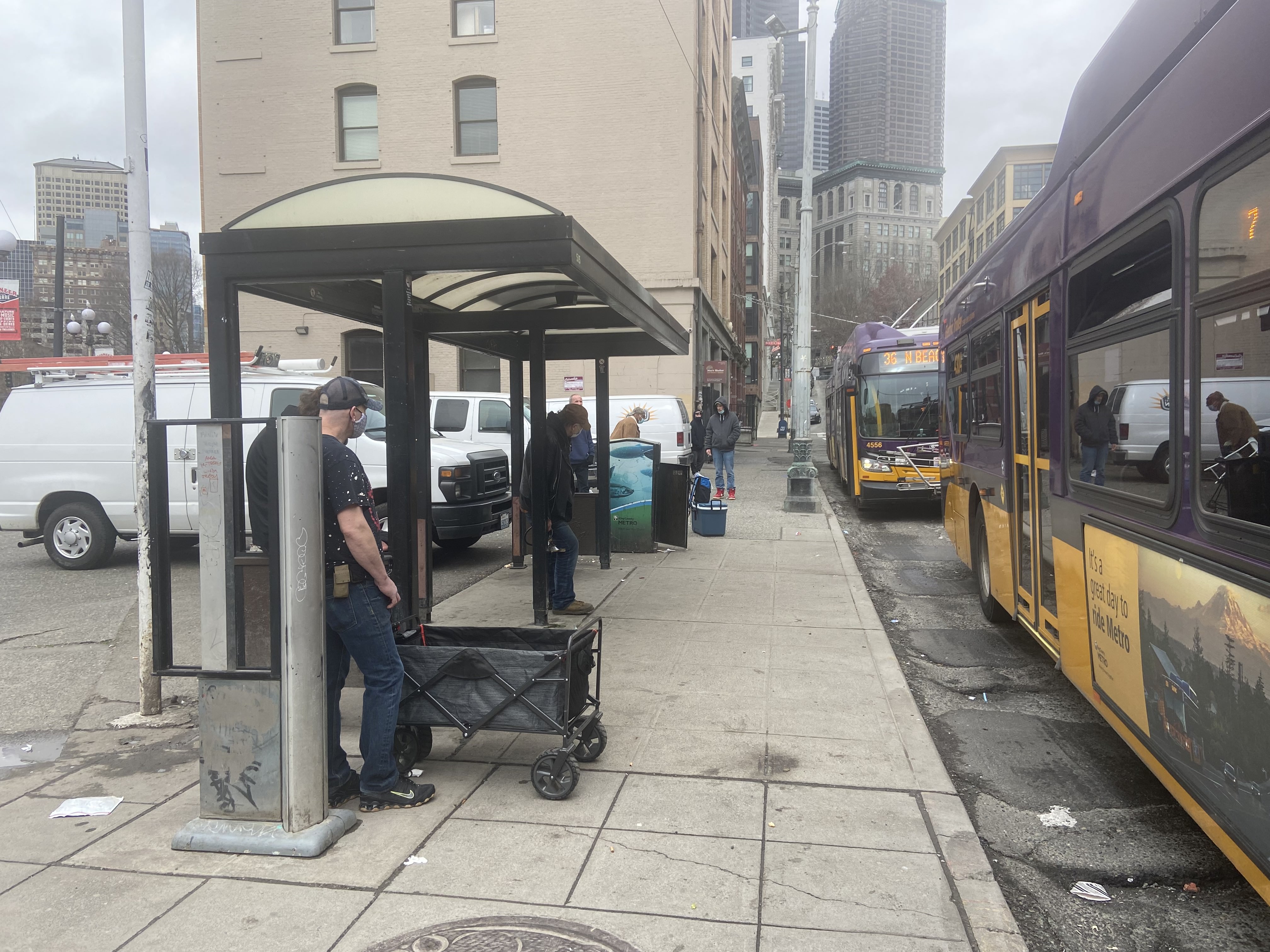 Una foto tomada mirando hacia la 3rd a la caseta de la parada de bus actual con un bus en la orilla de la acera.
