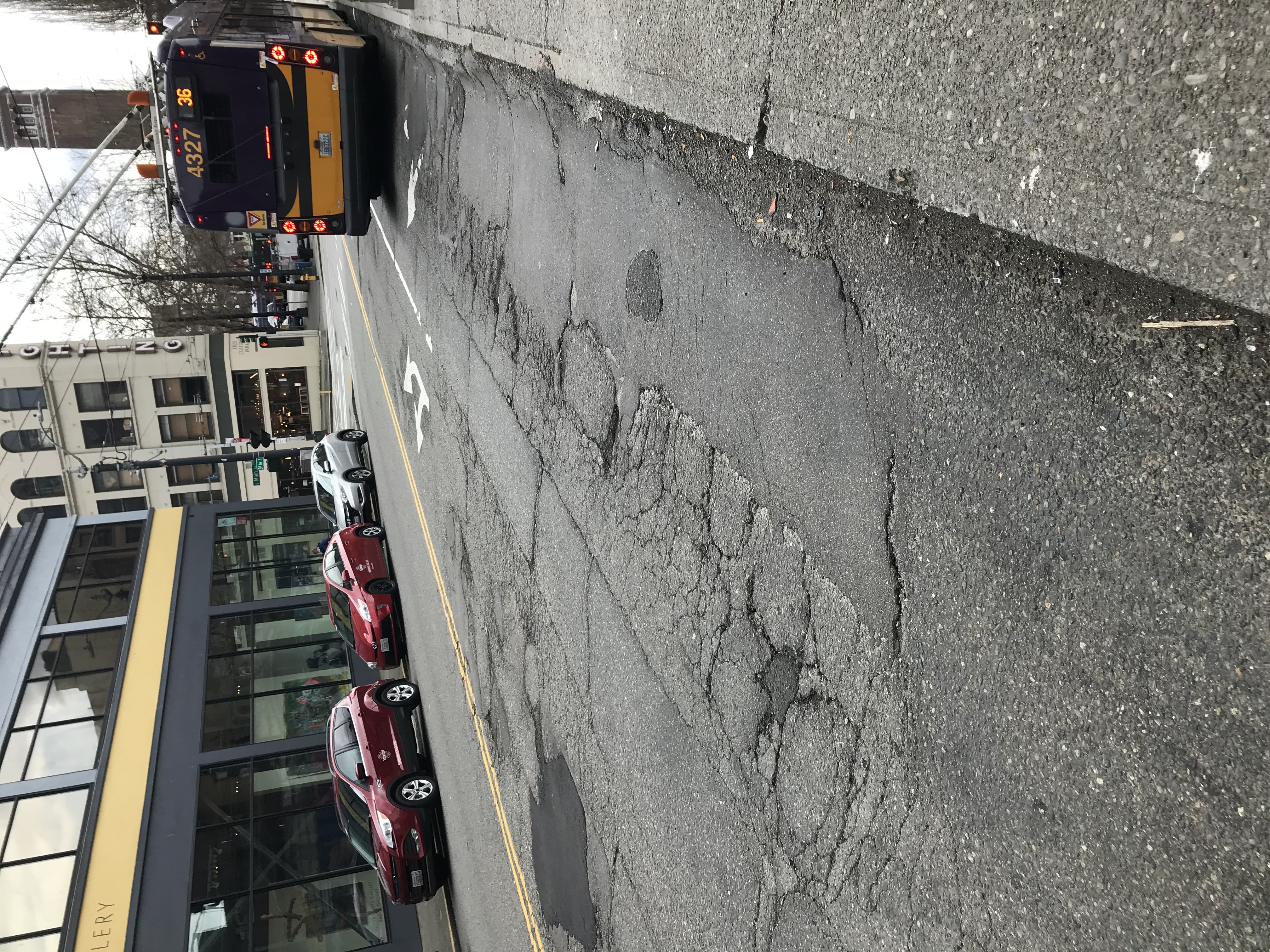 コンクリートで補修する必要がある既存バス停付近の道路の損傷個所の写真。