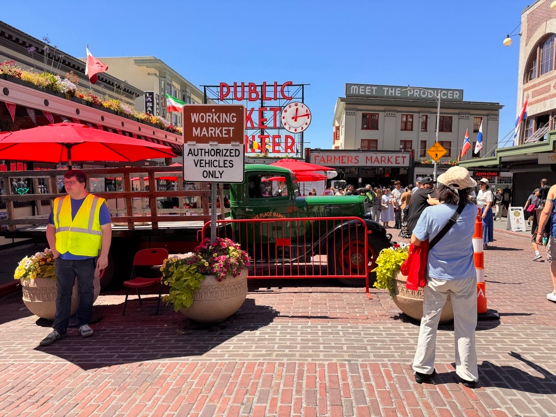 Planters and a historic truck narrow the entry to Pike Place Market, with a sign that says "Working Market Authorized Vehicles Only"