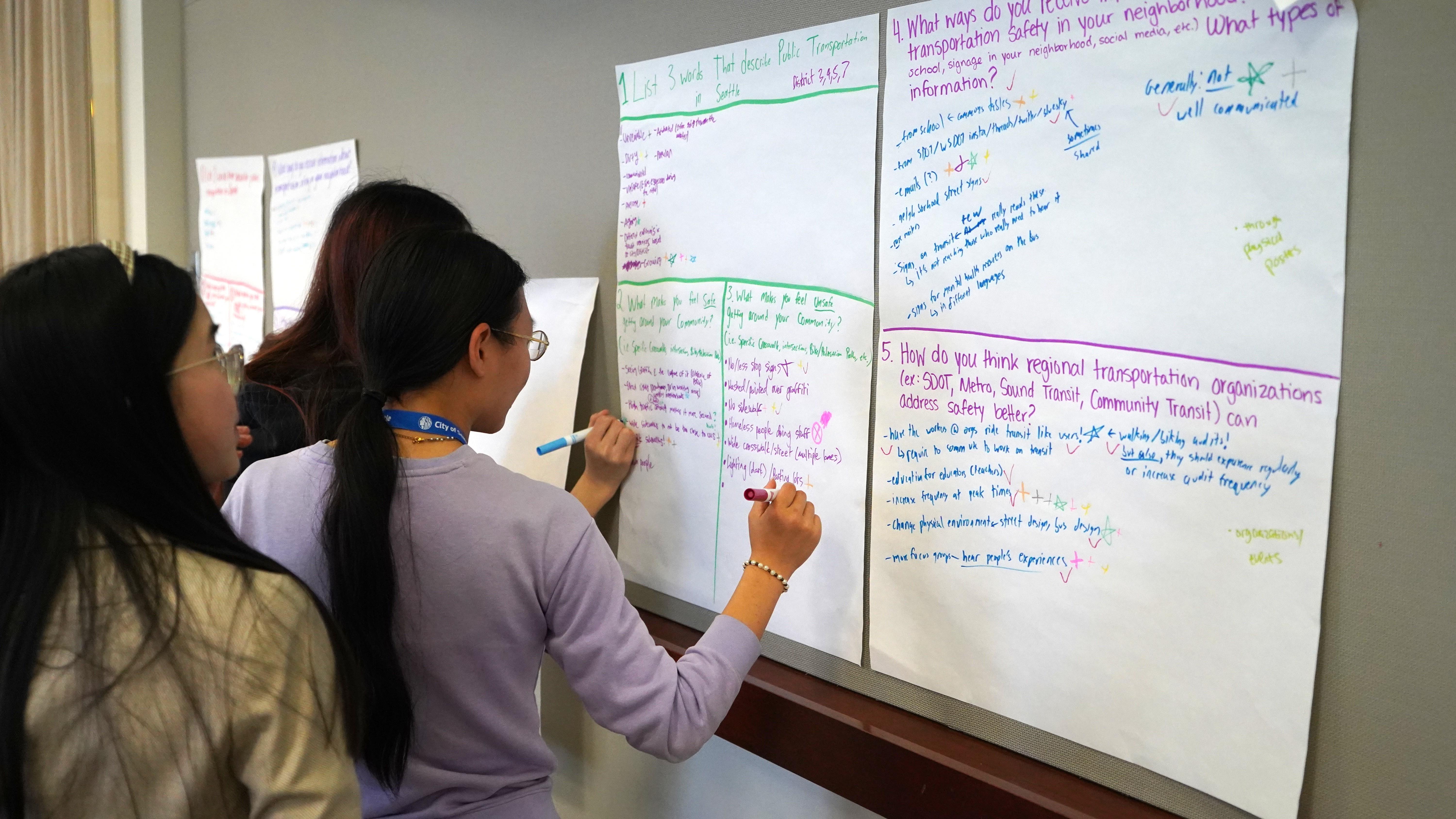 Three youth writing with markers on poster paper responses to questions about transportation safety