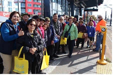 Seniors gathered around a outdoor light rail station smiling at the camera