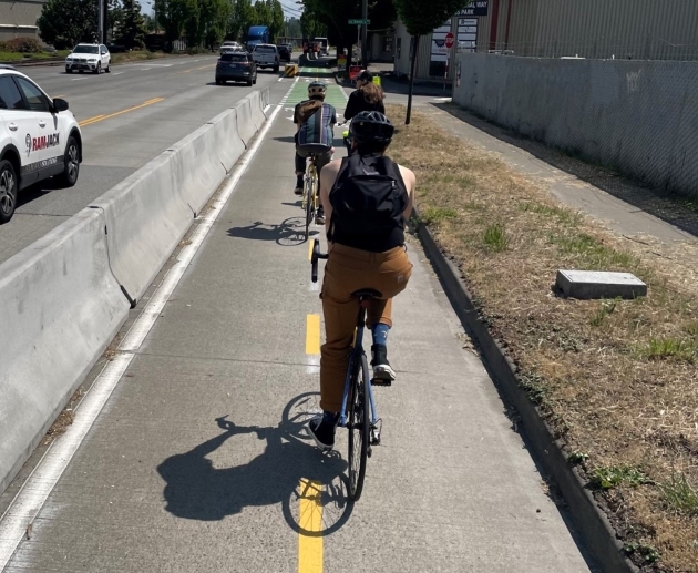 Three people riding their bikes along a protected bike lane along West Marginal Way