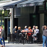 Six people enjoying a sidewalk cafe as passersby go about their business.