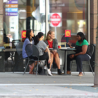 Four young women chatting while sitting at a sidewalk table.