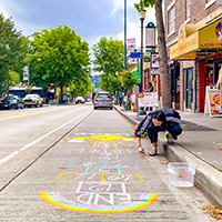 A young woman decorating a parking space with chalk for PARK(ing) Day.