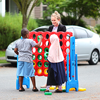 A woman playing an oversized game with two children in a street.