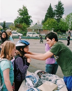 A young man helps a student with a bike helmet fitting