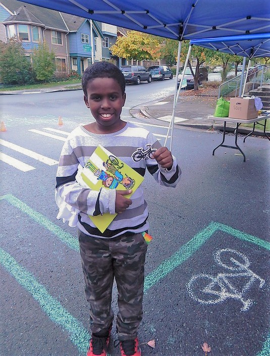 A smiling student holds a book and a bicycle sticker at a Safe Routes to School event