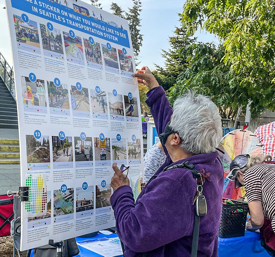 A woman at a community event putting stickers on a poster to provide feedback on transportation options